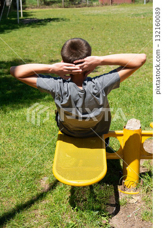 Teenager doing sit-ups outdoors on yellow exercise equipment. Healthy lifestyle and fitness. 132160089