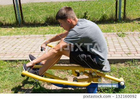 Teenager exercising outdoors on a sunny day, using a seated rowing machine. Teenager exercising outdoors on a sunny day, using a seated rowing machine. 132160092