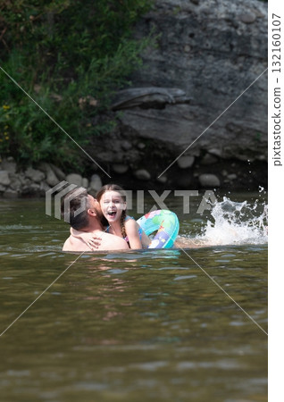 A joyful father and daughter playfully splash in a river, embracing in a moment of summer fun. A joyful father and daughter playfully splash in a river, embracing in a moment of summer fun. 132160107