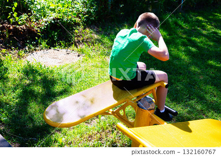 Young boy exercising outdoors on yellow fitness equipment. 132160767