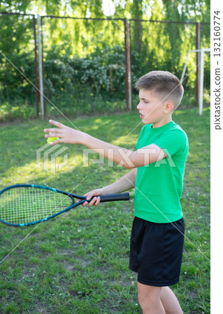 Young boy playing badminton outdoors, tossing the shuttlecock before serving. 132160774