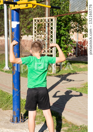 Boy flexing muscles at outdoor gym. Showing strength and fitness. Boy flexing muscles at outdoor gym. Showing strength and fitness. 132160776