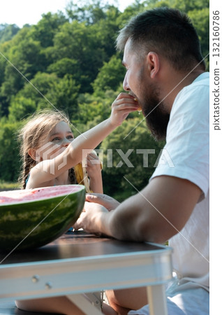 A father and daughter enjoy a picnic outdoors, sharing fruit and spending quality time together. 132160786