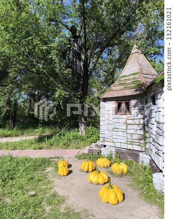 Eerie Halloween Display Stone Cottage, Pumpkins, Ghoulish Figure Among Verdant Trees 132161021