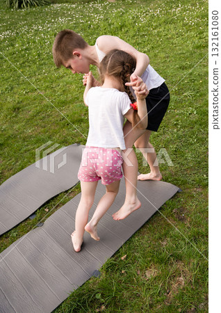 Brother and sister playing outdoors on exercise mats. Fun sibling playtime in the grass. Brother and sister playing outdoors on exercise mats. Fun sibling playtime in the grass. 132161080