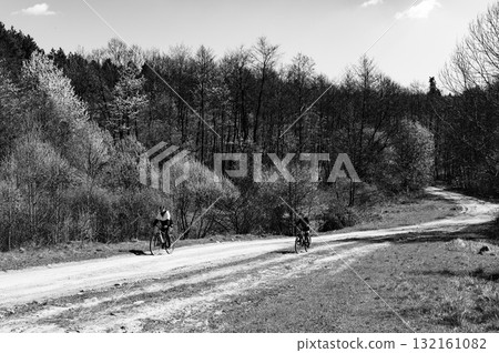 Two cyclists enjoy a sunny ride on a country road, surrounded by trees. A peaceful and scenic escape. Two cyclists enjoy a sunny ride on a country road, surrounded by trees. A peaceful and scenic escape. 132161082