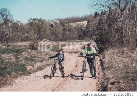 Father and son walking bikes on a country road, enjoying a sunny day outdoors. 132161085