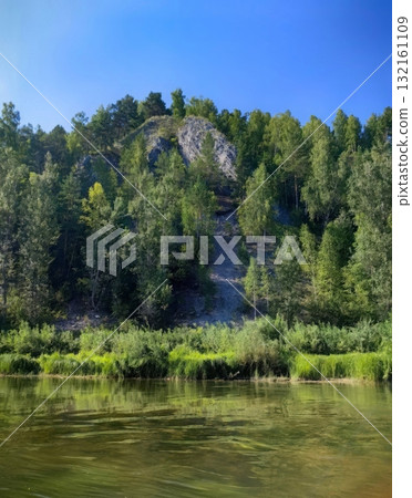 Idyllic Riverbank Scene Lush Green Forest and Clear Blue Sky Landscape, Nature s Serenity. 132161109