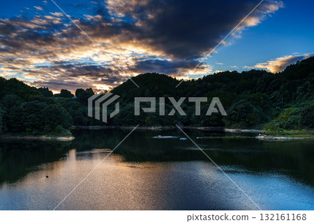 奈良布目水壩布目湖上空的中秋日落空。烏雲籠罩在金色的光芒中,天空倒映在布目湖上。 奈良布目水壩布目湖上空的中秋日落空。烏雲籠罩在金色的光芒中,天空倒映在布目湖上。 132161168