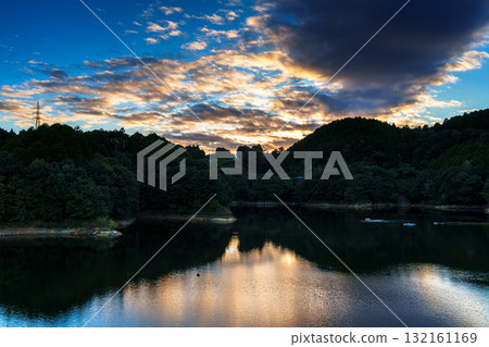 Mid-autumn sunset sky above Lake Nunome at Nunome Dam in Nara. Dark clouds framed in golden light and the sky reflected in Lake Nunome. 132161169