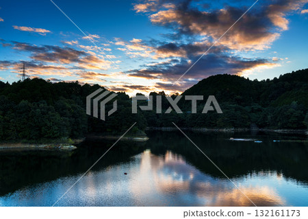 Mid-autumn sunset sky above Lake Nunome at Nunome Dam in Nara. Dark clouds framed in golden light and the sky reflected in Lake Nunome. 132161173
