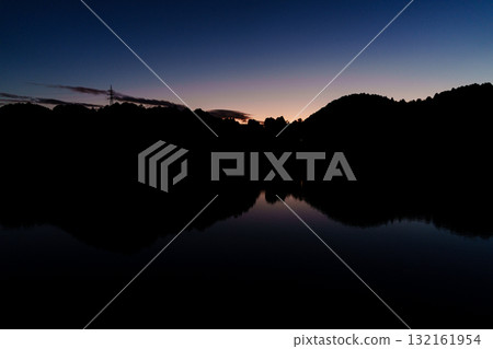 Mid-autumn sunset over Lake Nunome at Nunome Dam in Nara. The sunset and blue sky remain on the mountainside. 132161954