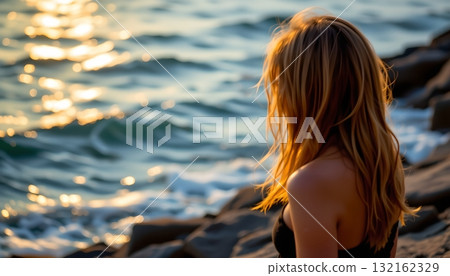 A serene beach sunset scene, featuring a woman gazing into the ocean from a rocky outcropping near the water's edge A serene beach sunset scene, featuring a woman gazing into the ocean from a rocky outcropping near the water's edge 132162329