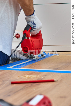 repairman using handheld electric jigsaw and cutting hole for the sink in the kitchen countertops 132162683
