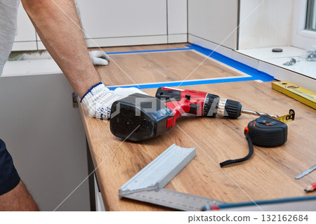 repairman working on a new kitchen installation and using electric drill 132162684
