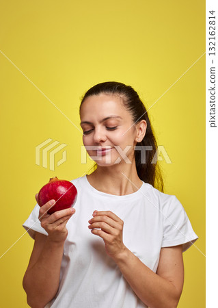 Beautiful happy woman holding pomegranate on yellow background Beautiful happy woman holding pomegranate on yellow background 132162814