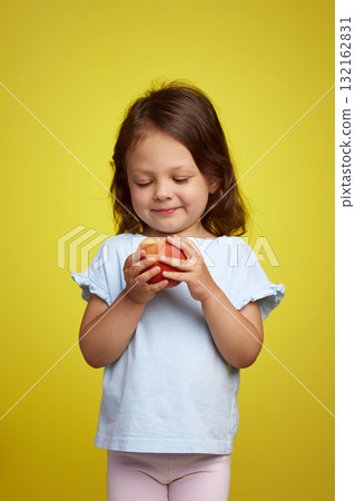 Portrait of brunette little child girl with peach on yellow background 132162831
