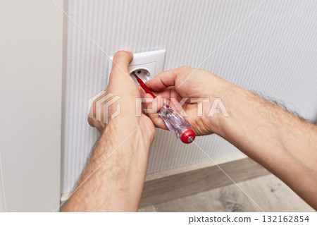 male hands installing electrical socket in white plastic frame with a screwdriver at home 132162854