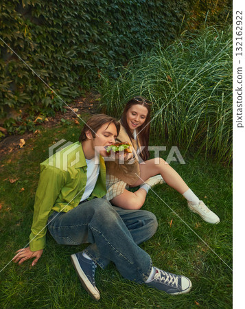 Young couple sitting on grass enjoying street food and carefree time together Young couple sitting on grass enjoying street food and carefree time together 132162922
