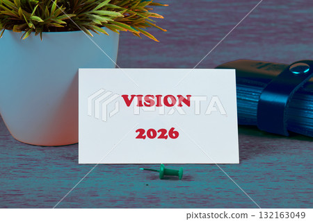 A card displaying the title Vision 2026 sits on a rustic wooden table beside a small potted plant 132163049