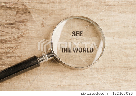 A magnifying glass lies on a wooden surface, focusing on the words that invite exploration and curiosity. It symbolizes the joy of uncovering hidden sights in the world 132163086