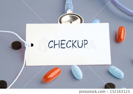 A health checkup reminder card sits among various pills, emphasizing the need for regular medical assessments to ensure overall well-being and early disease detection 132163123