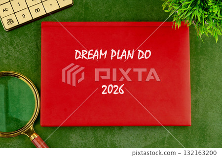 A bright red notebook titled Dream Plan Do is placed on green textured surface, surrounded by a magnifying glass and a small plant, inspiring future planning for 2026 A bright red notebook titled Dream Plan Do is placed on green textured surface, surrounded by a magnifying glass and a small plant, inspiring future planning for 2026 132163200