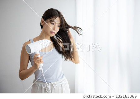 一位年輕的女士用吹風機吹乾頭髮 132163369