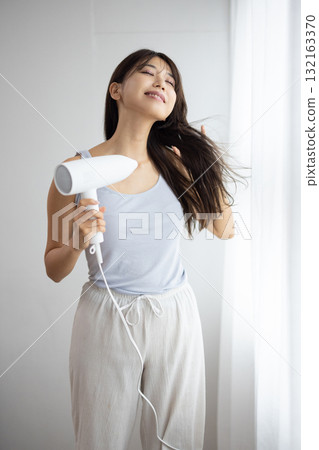 一位年輕的女士用吹風機吹乾頭髮 132163370
