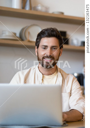 Bearded man working on his laptop in the kitchen 132163475