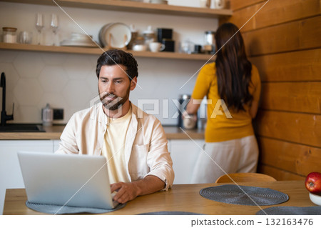 Bearded man working on his laptop in the kitchen Bearded man working on his laptop in the kitchen 132163476