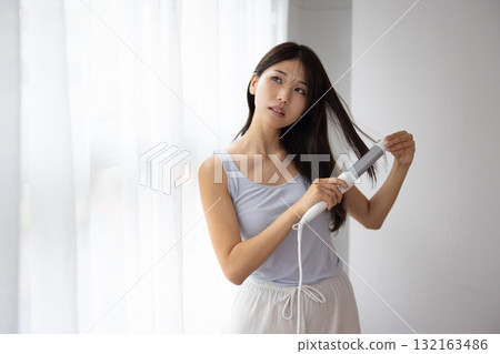 Young woman using a hair iron Young woman using a hair iron 132163486