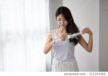 Young woman using a hair iron 132163489