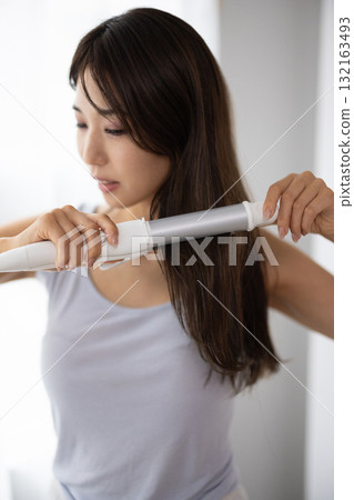 Young woman using a hair iron 132163493