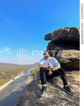 Man Sitting on Cliff Overlooking River and Valley 132163653