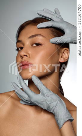 Doctor hands in gloves examining woman face with calm precision and trustful emotion 132164700