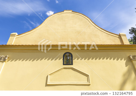 Yellow baroque facade with religious figure and blue sky 132164795