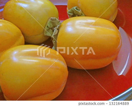 Saijo persimmons mixed together. A simple photo of the orange Saijo persimmons with a red background. 132164889