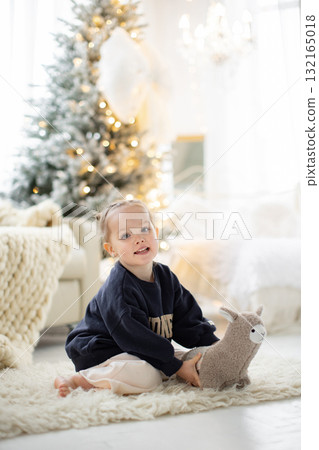 A young girl smiles while holding a stuffed animal in front of a Christmas tree. A young girl smiles while holding a stuffed animal in front of a Christmas tree. 132165018