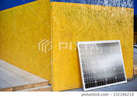 Solar panel against vibrant wall painted in blue and yellow colors of Ukrainian flag. Scene symbolizes integration of sustainable renewable energy solutions within culturally significant context. 132166218