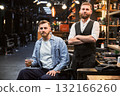 Brutal confident man satisfied with his new look. Experienced barber showing result of his work. Two bearded men smiling to camera. 132166260