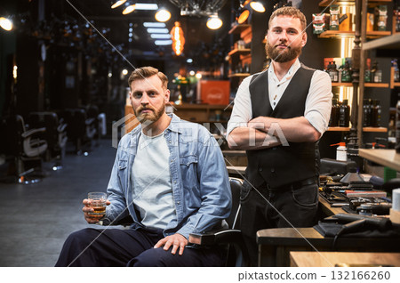 Brutal confident man satisfied with his new look. Experienced barber showing result of his work. Two bearded men smiling to camera. 132166260