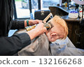 Little boy getting his first haircut. Back view of hairdresser shaving head. Cute client in barbershop. 132166268