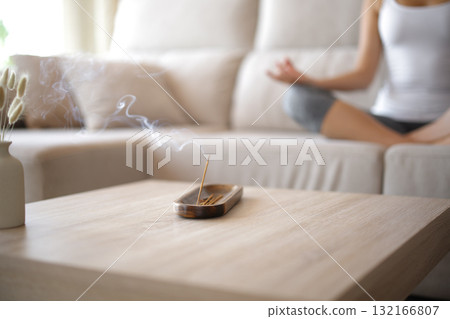 Incense stick burning in foreground and woman doing yoga 132166807