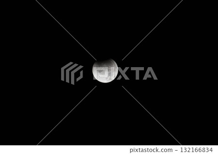 A partial lunar eclipse of the moon floating in the pitch-black night sky 132166834