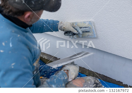 Worker applying plaster to building wall with trowel 132167972