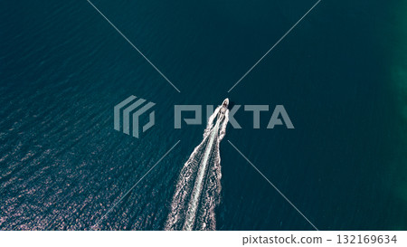 Top down drone of speedboat carving clean wake across teal sea near rocky coast minimal copyspace background 132169634