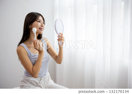 A young woman applying makeup while looking at a hand mirror A young woman applying makeup while looking at a hand mirror 132170134