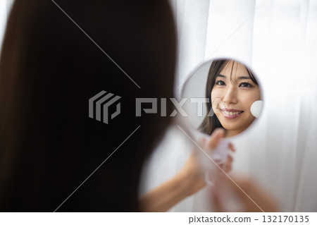 A young woman applying makeup while looking at a hand mirror A young woman applying makeup while looking at a hand mirror 132170135