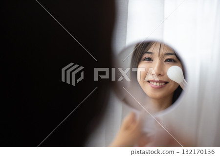 A young woman applying makeup while looking at a hand mirror A young woman applying makeup while looking at a hand mirror 132170136